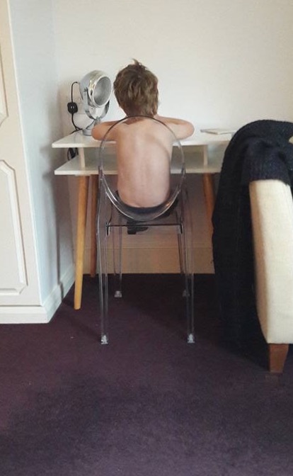 Topless boy at desk his back to camera. 